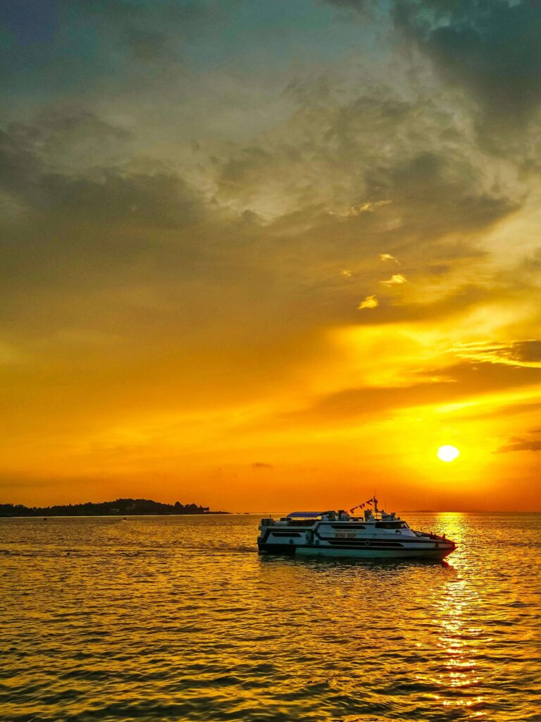 A boat sails on calm waters during a vibrant sunset, highlighting the beauty of Batam, Riau Island.