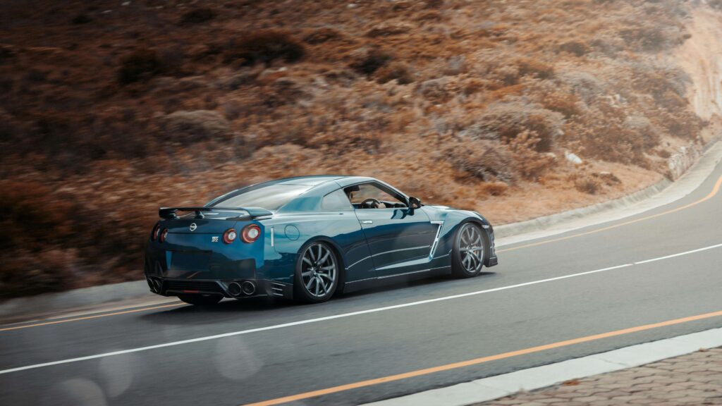 A blue sports car speeds along a scenic mountain road, highlighting the need for the best petrol to maintain fuel efficiency.