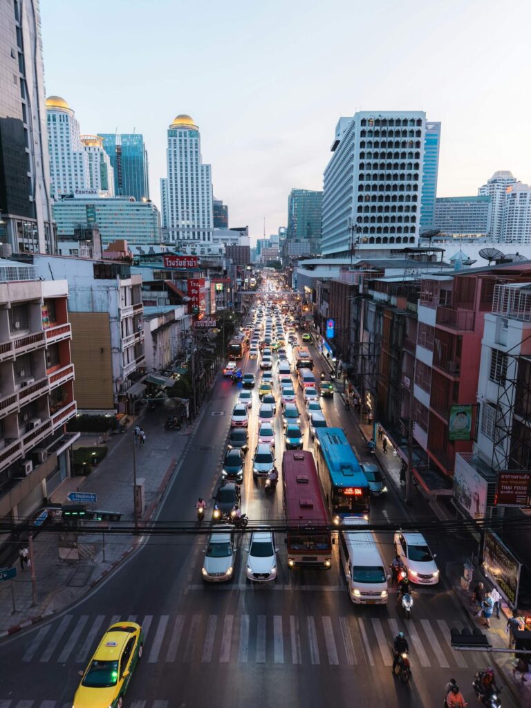 A vibrant Bangkok street scene with numerous cars and buses, highlighting the busy atmosphere during peak travel hours.